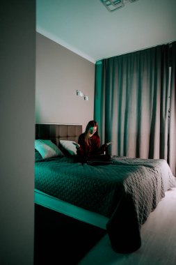 Genç kadın gün boyunca küçük bir odada yatarken dizüstü bilgisayarda ders çalışıyor.