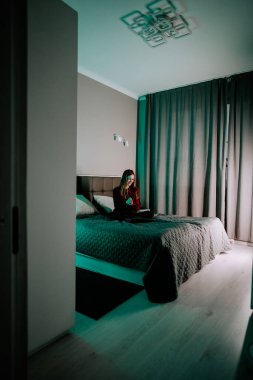 Genç kadın akşamları evdeki modern bir yatak odasında yatarken dizüstü bilgisayarda ders çalışıyor.