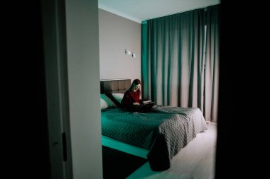 Genç kadın, akşam saatlerinde modern odada dizüstü bilgisayarla ders çalışıyor.