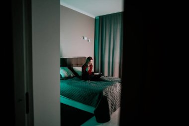 Genç bir kadın, akşam saatlerinde odasında yatarken dizüstü bilgisayarda ders çalışır.