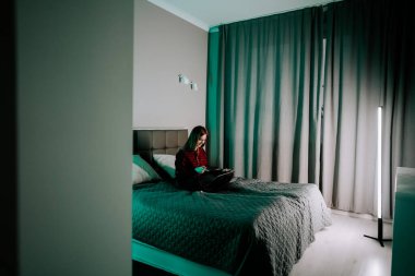 Genç bir kadın akşam saatlerinde odasında dizüstü bilgisayarla ders çalışıyor.