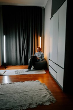 Genç bir kadın, sessiz bir odada, sıcak ışıklandırmalı bir kanepe üzerine kitap okumaktan hoşlanıyor.