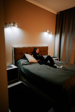 Genç kadın, oturma odasında uzaktan kumandayla televizyon izlerken kanepede dinleniyor.