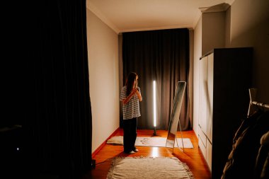 Akşam saatlerinde aynanın yanında saç maşası kullanan bir kadın.