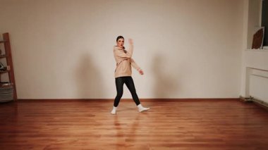 Bir kadın dans salonunda kapüşonlu ve çoraplı dans ediyor.