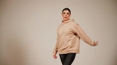 Canlı bir performans sırasında, bir salonda bej kapüşonlu ve siyah pantolonlu bir kadın dans eder.