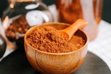 Mutfak tezgahında kepçeli tahta kasede kakao tozu ve arka planda kavanozlar.