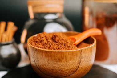 Kakao tozu, arka planda bir kaşık ve konteynırla ahşap bir kasede duruyor.