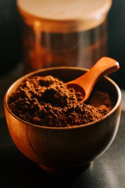 Tahta kasede kakao tozu kepçeli ve kavanozu yumuşak ışık ayarlı.