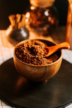 Kakao tozu ahşap bir kasede, siyah bir masada bir kaşıkla, rahat bir mutfak ortamında.