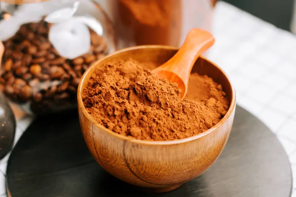 Tahta bir kasede kakao tozu, yakınlarda kahve çekirdekleri olan bir masada.