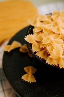 Ahşap bir yüzeyde, siyah bir kasede, etrafa saçılmış parçalarla makarna.