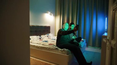 Arkadaşların gece rahat bir odada renkli ışıklarla selfie çekmesi.