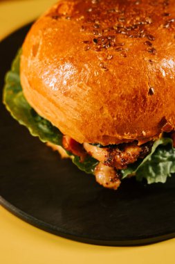 Sarı arka planda marullu sulu burger öğle veya akşam yemeği için siyah tabakta servis edilir.