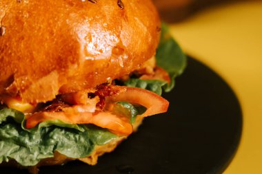 Salatalı ve domatesli sulu burger, yemek anı için sarı arka planda.