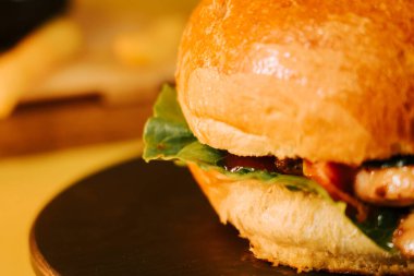 Sarı arka planda sulu bir burger ve öğle yemeğinde yenecek taze malzemeler.