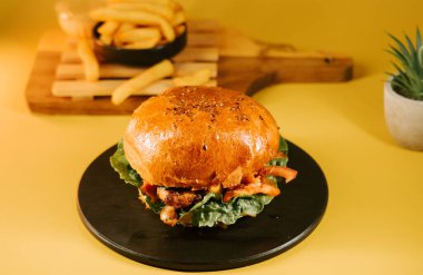 Sulu burger siyah bir tabakta oturur. Arka planda sarı arka plan ve patates kızartması vardır.