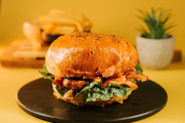 Siyah bir tabakta servis edilen sulu hamburger, sarı bir arka plan ve uzakta patates kızartması.