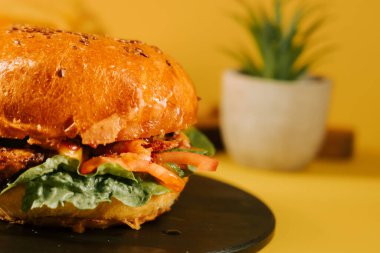 Sarı arka planda marul ve domatesli sulu burger.