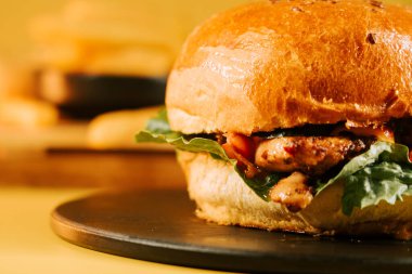 Koyu bir tabağa yerleştirilmiş sulu burger, açık sarı bir zemin üzerinde basit elementlerle.