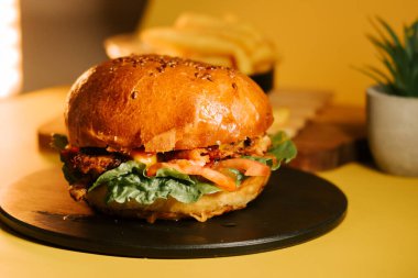 Sulu burger, sarı arka plan ve yan öğeleri olan siyah bir tabağa oturur.