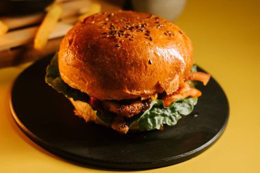 Salatalı ve domatesli sulu burger, sarı arka planda.