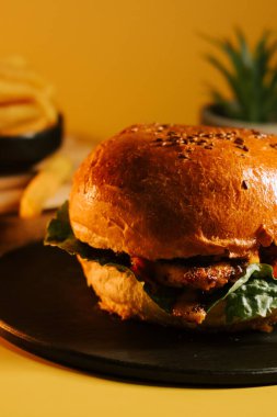 Sulu burger, siyah tabakta servis edilir. Sarı arka plan, patates kızartması ve yeşillik.
