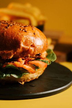 Sarı zemin üzerinde taze yapılmış burger ve yanında da sıcacık patates kızartması.