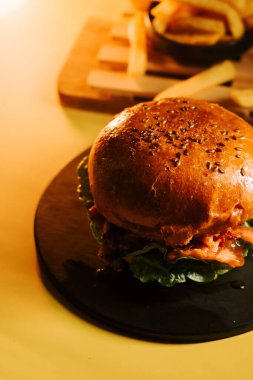 Siyah bir tabakta servis edilen sulu hamburger ve sarı masada patates kızartması.