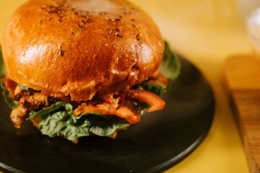 Sarı arka planda sulu bir burger. Taze malzemeler ve her aşerme için lezzetli malzemeler var.