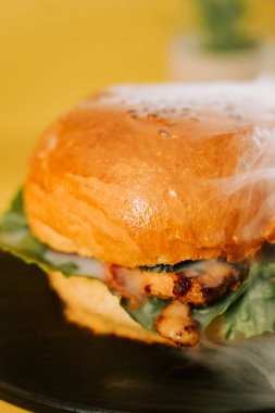 Sulu burger sarı arka planda, öğle yemeğinde marul ve ızgara tavukla oturur.