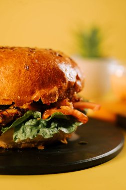 Sarı arka planı olan sulu bir hamburger ve arka planda bulanık nesneler.