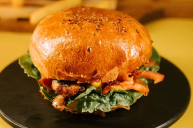 Yuvarlak bir tabağa yerleştirilmiş sulu hamburger ve parlak sarı bir arka planda taze malzemeler.