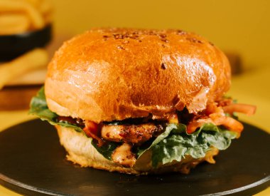 Salatalı ve domatesli sulu burger, sarı arka planda bir tabağa konur.