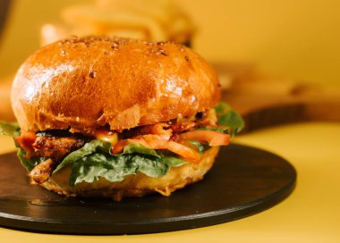 Yuvarlak tabakta salata ve domatesli sulu burger, sarı bir arka plan ve sıradan bir ortam.