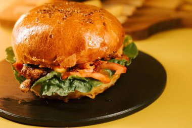 Sarı zemin ve taze malzemelerle dolu bir tabakta dinlenen sulu bir burger.