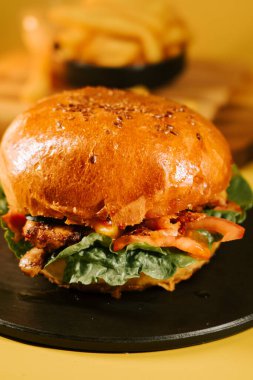 Sulu burger, yeşil marul ve domatesli siyah bir tabakta servis edilir.