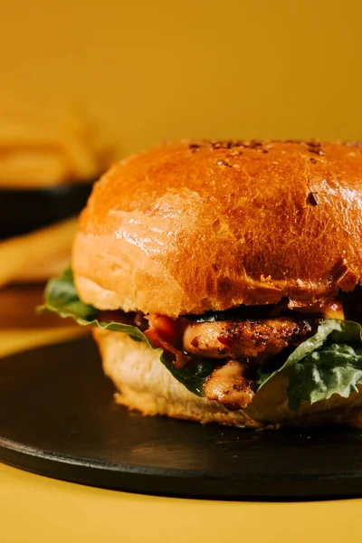 Parlak sarı bir arka planda siyah bir tabağa taze malzemeler konmuş sulu hamburger.