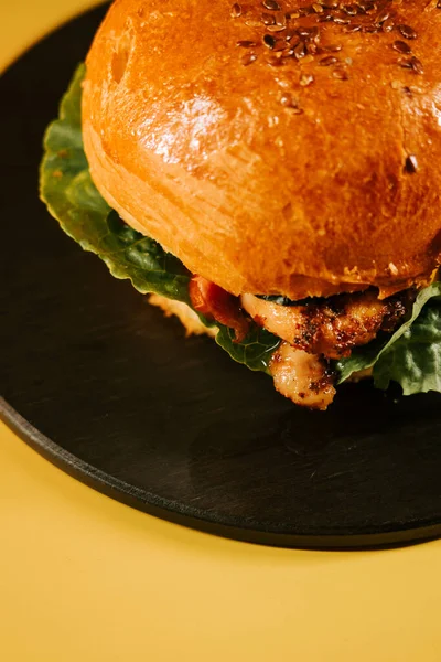 Siyah bir tabakta servis edilen sulu hamburger, sarı arka planda taze malzeme ve doku içeriyor.