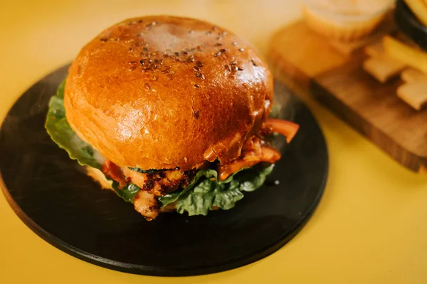 Sulu burger siyah bir tabakta oturuyor, parlak sarı bir zemin üzerinde, tadını çıkarmaya hazır.