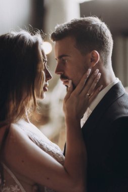 Bir çift, düğün sırasında, hafif ışıklandırılmış bir mekanda samimi bir anı paylaşıyor.