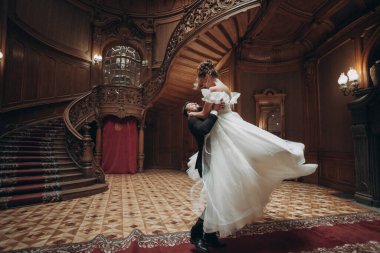 Büyük salonda zarif merdivenleri ve ahşap süslemeleri olan çift dans ediyor.