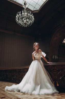 Beyaz elbiseli kadın, tarihi bir binada balkonun yanında avizeyle poz veriyor.