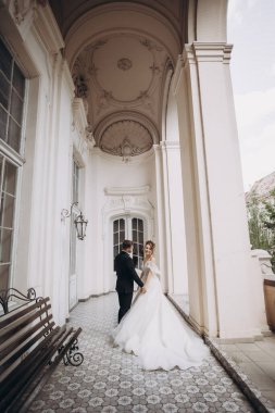 Çift, bir düğün sahnesinde zarif mimari ile işaretlenmiş tarihi bir binada birlikte duruyor.