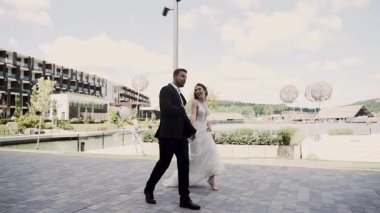 Çiftler, güneşli bir havada göl kenarında bir düğün yerinde yürür.