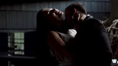 Çiftler düğün gecelerinde yumuşak ışıklandırmanın altında kırsal bir mekanda öpüşürler.