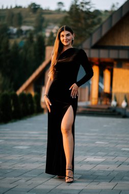 Siyah elbiseli genç bir kadın akşam vakti açık havada duruyor.