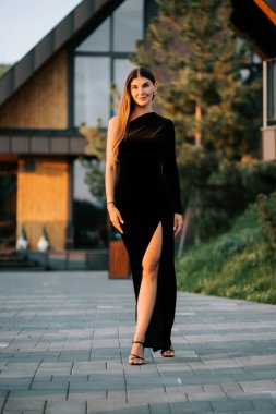 Siyah elbiseli bir kadın akşamleyin modern bir binanın yanında yürür.