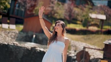 Kadın, güneşli bir açık havada dalgalanan bir suyun yanında mutlu bir şekilde el sallıyor.