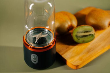 Mutfaktaki tahta kesme tahtasında kivi ile meyve suyu yapmak için taşınabilir blender.